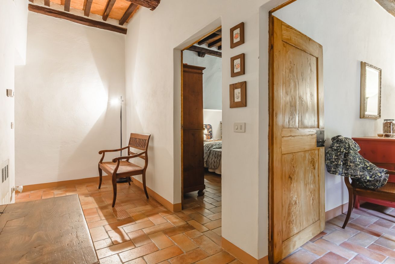 A room with a wooden door, a chair, and a bed with a patterned bedspread.