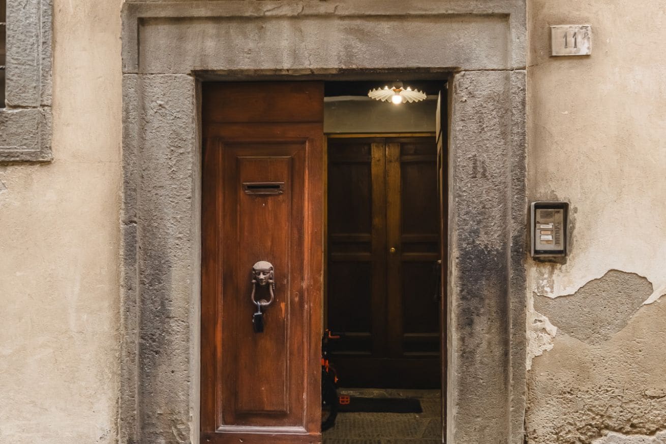 A wooden door with a metal handle and a keyhole, set in a stone wall with a number plaque above it.