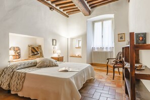 A bedroom with a large bed, a wooden chair, a radiator, and a window with curtains. - Casa Teresa - Authentic Tuscan Charm in the Heart of Cortona (Cortona)