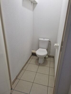 A small, narrow bathroom with a white toilet, a toilet paper holder, and a tiled floor. - Beautiful, bright, and quiet 2-bedroom apartment near Toulouse (Castanet-Tolosan)