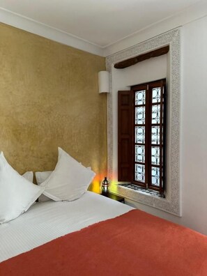 Habitació d'hotel amb un llit, una finestra amb baranes de ferro decoratives i una làmpada penjada a la paret.