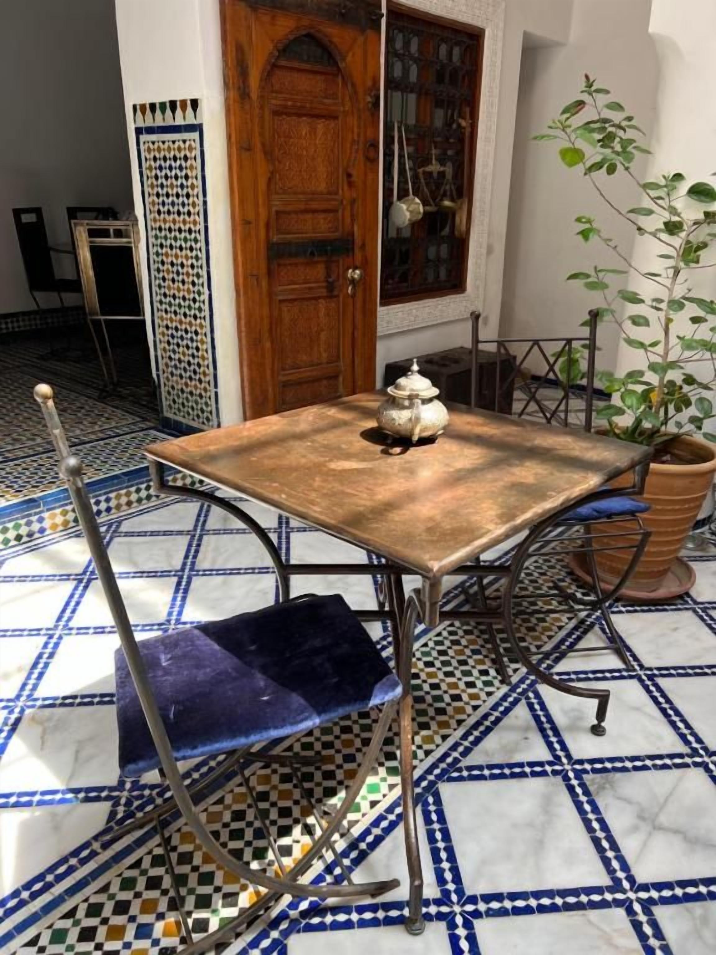 A dining table with a vintage design, a blue cushioned chair, and a potted plant.