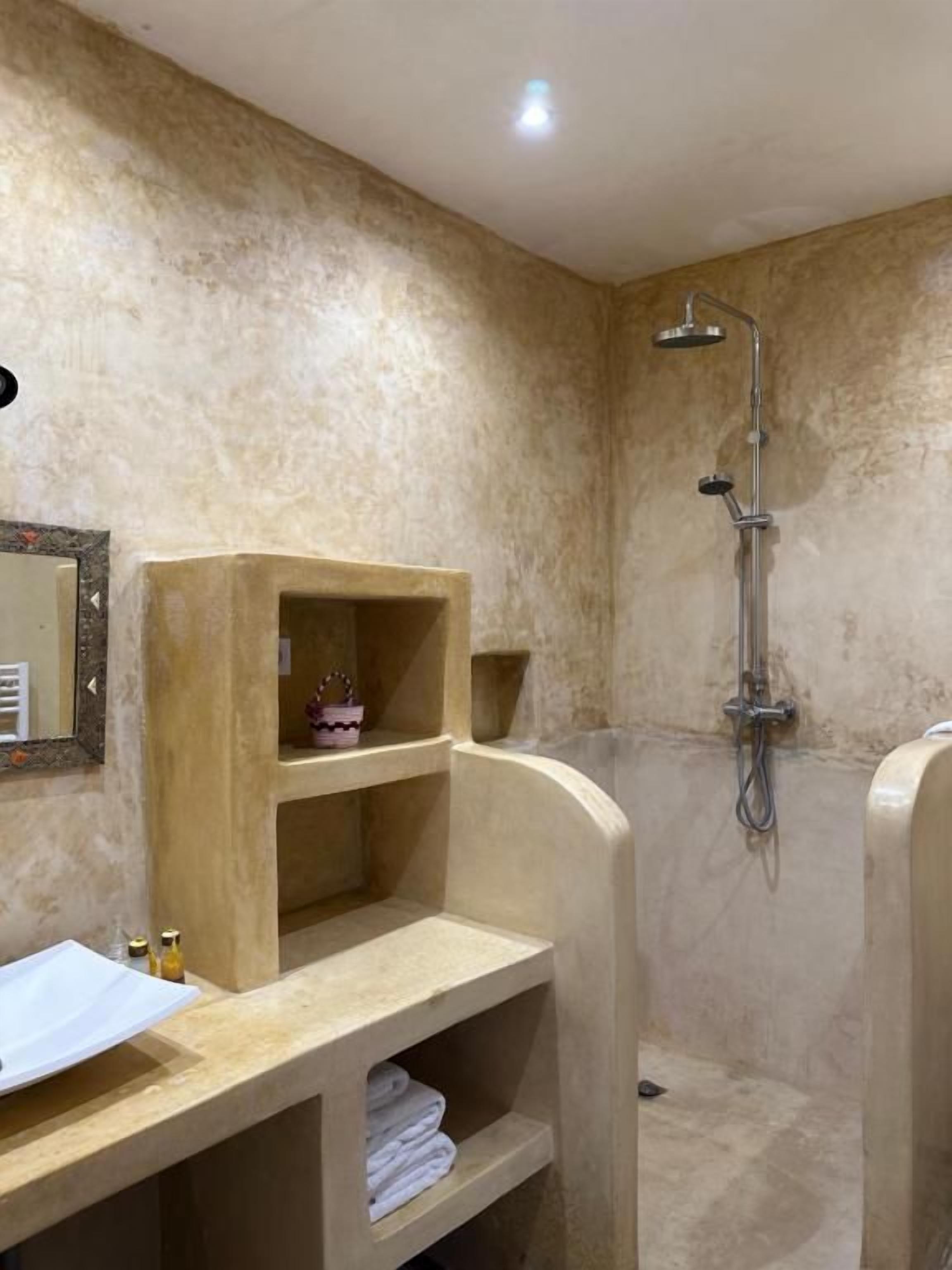 Un baño con ducha, tocador con espejo y repisas con toallas.