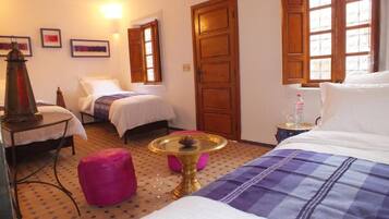 A hotel room with two beds, a small table with a vase, a lamp, and a window with curtains.