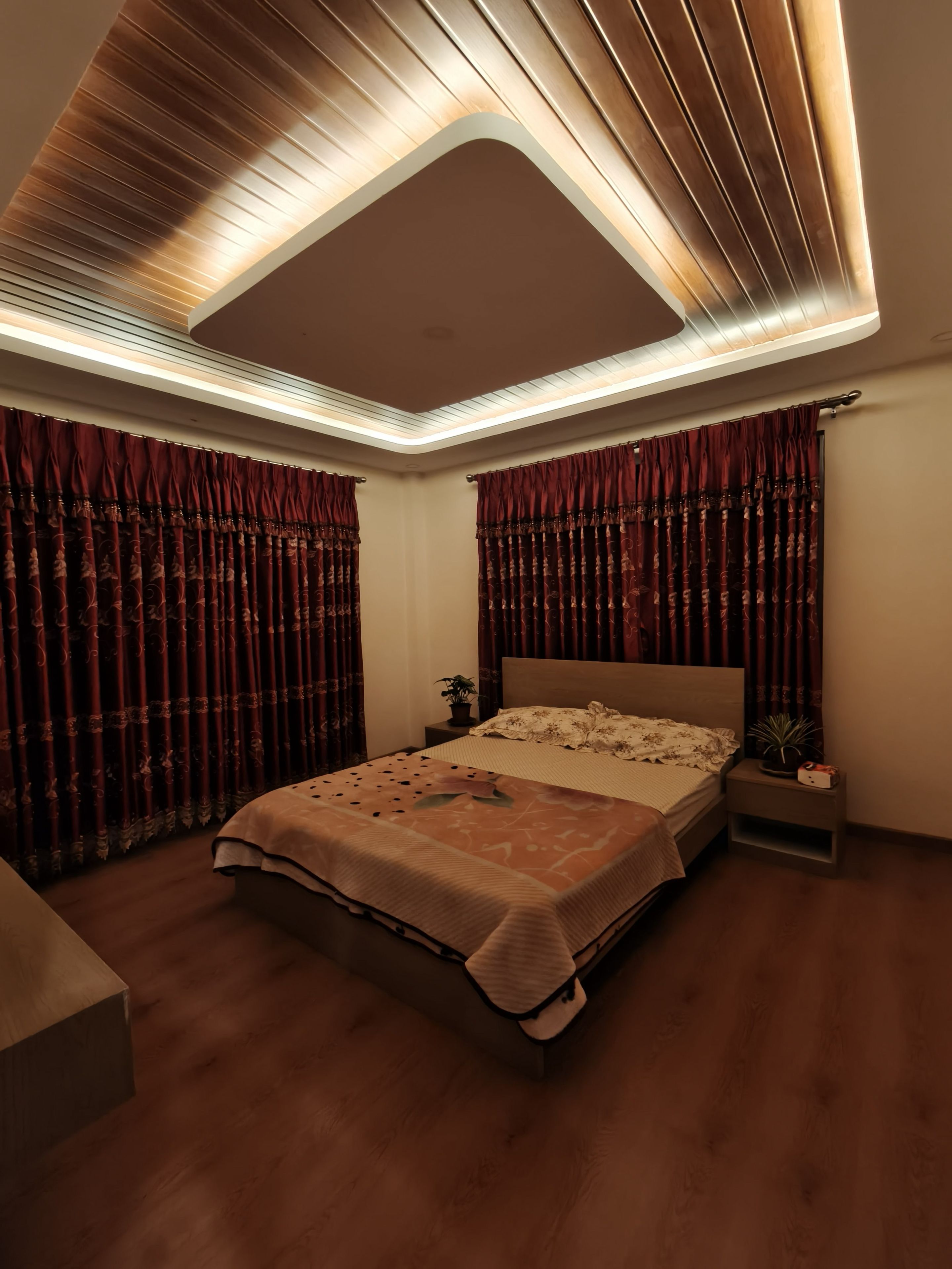 Un dormitorio con cama, mesitas de noche, una planta en maceta e iluminación empotrada en el techo.