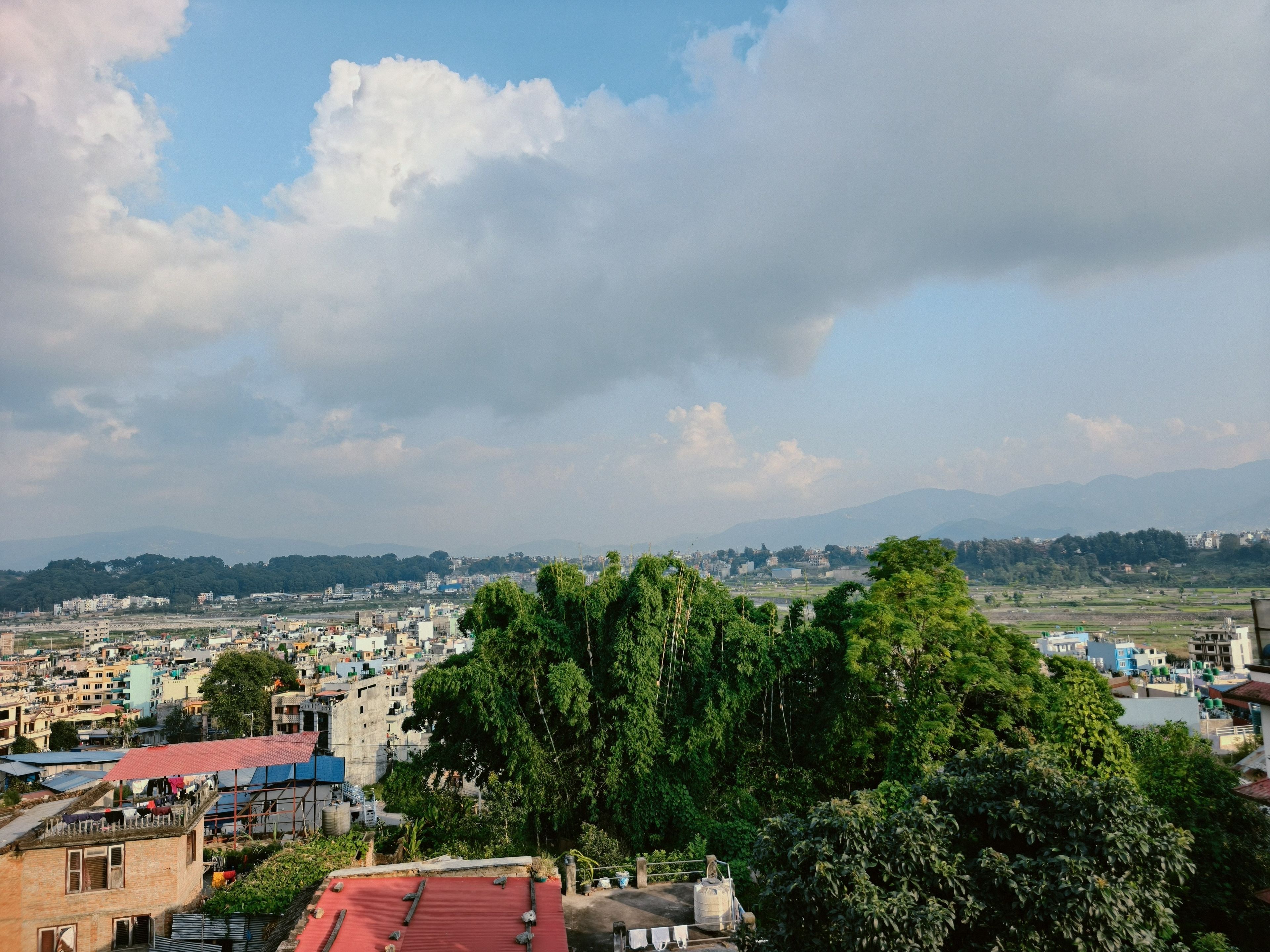 A cityscape with buildings, trees, and mountains in the background.