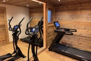 A gym with three elliptical machines and one treadmill, wooden walls, and a window. - Luxury Mountain Chalet with Jacuzzi, Sauna & Hammam near Mont Blanc (Saint-Gervais-les-Bains)