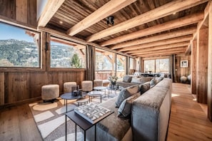 A spacious room with a wooden ceiling, large windows, a sofa, and a coffee table. - Luxury Mountain Chalet with Jacuzzi, Sauna & Hammam near Mont Blanc (Saint-Gervais-les-Bains)