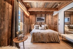 A bedroom with a wooden ceiling, a bed with a grey duvet, a bedside table with a candle, and a framed picture on the wall. - Luxury Mountain Chalet with Jacuzzi, Sauna & Hammam near Mont Blanc (Saint-Gervais-les-Bains)