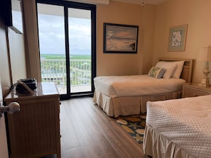 Habitación de hotel con balcón, una cama, un escritorio con teléfono y una mesita de noche con lámpara.