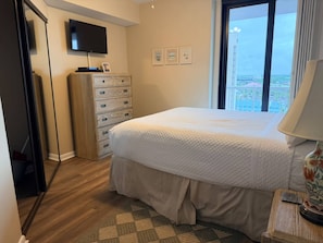 Una habitación de hotel con cama, cómoda, televisor y ventana con vistas.