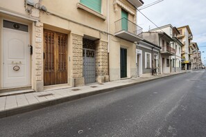 Vista del carrer amb una filera d'edificis, incloent-hi un edifici amb un balcó i una porta amb una placa amb número.