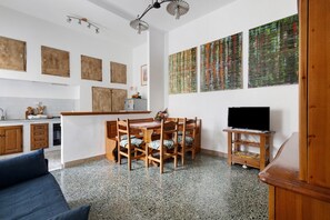 Eine moderne Küche mit Holzschränken, ein Essbereich mit Holztisch und -stühlen, ein Fernseher auf einem Holzboden und abstrakte Kunst an den Wänden.