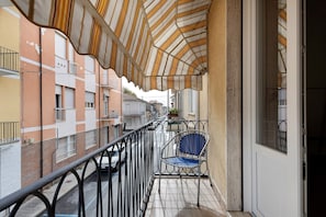 Un balcó amb barana metàl·lica, una cadira blava i un tendal estriat.