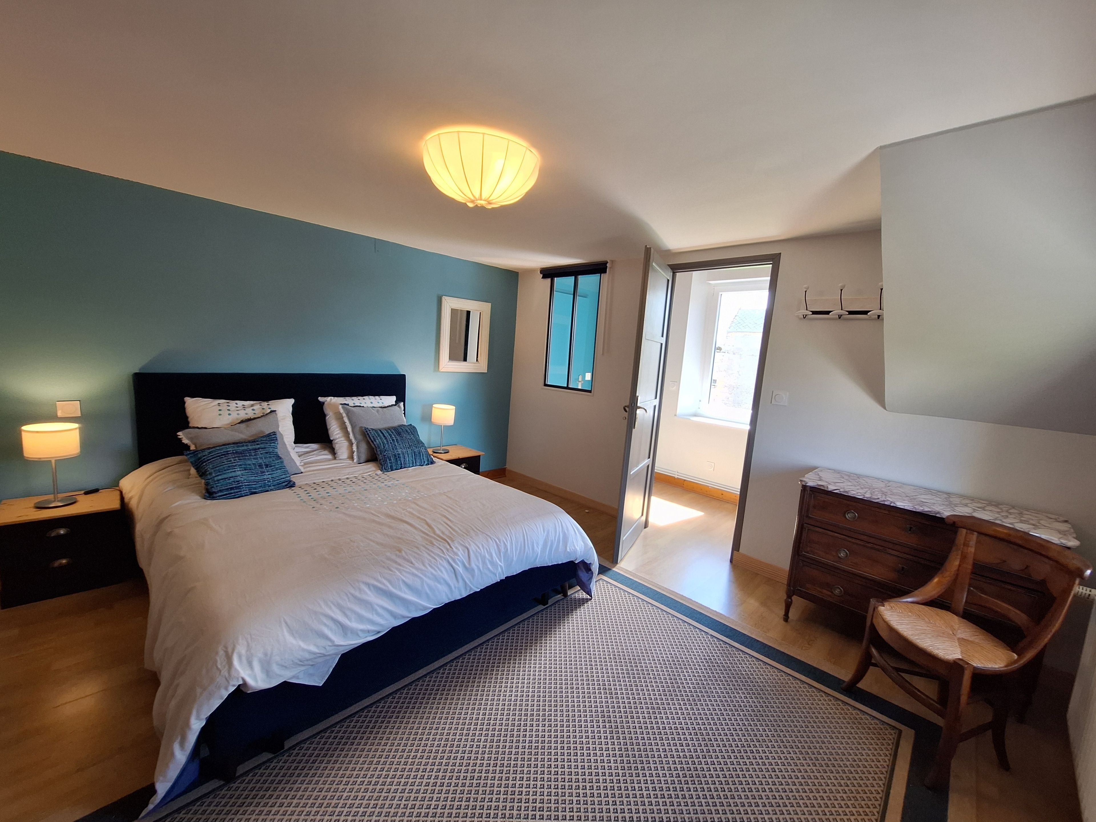 Une chambre à coucher comprenant un lit, des tables de chevet, une commode, une chaise et un luminaire au plafond.