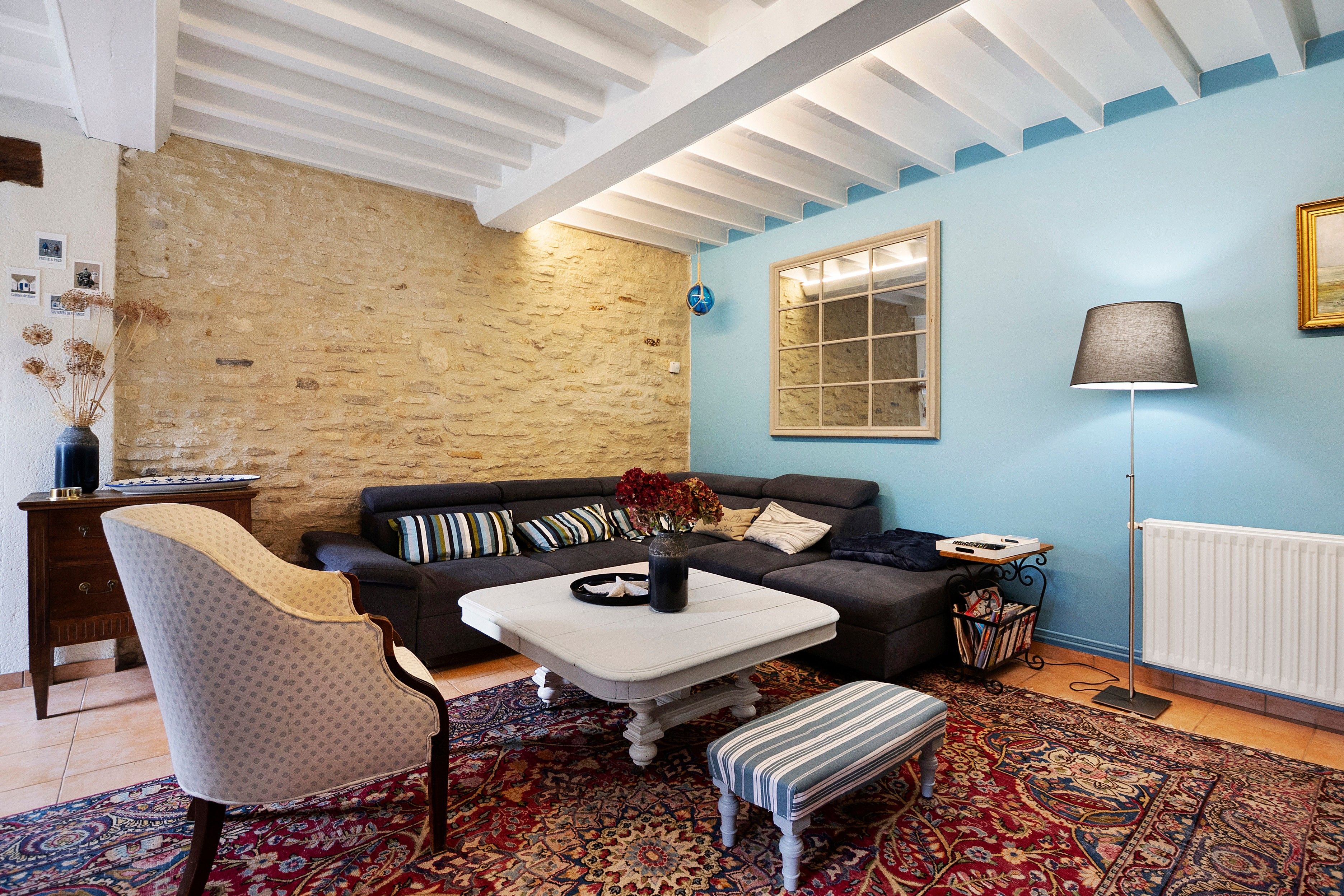 A living room with a stone wall, a blue wall, a window, a lamp, a sofa, a chair, a coffee table, and a patterned rug.
