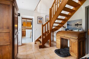 A staircase leading to a second floor, a kitchen area with wooden cabinets, and a dining table with chairs.