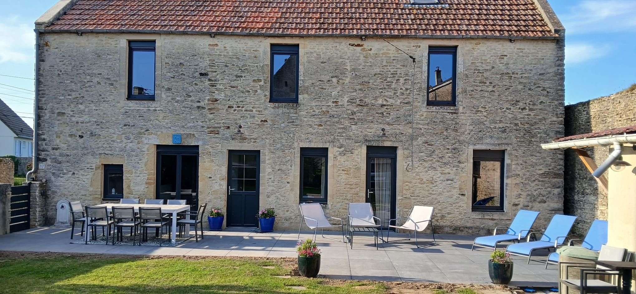 Ein Steinhaus mit Ziegeldach, einer Terrasse mit Sitzgelegenheiten und einem kleinen Garten.
