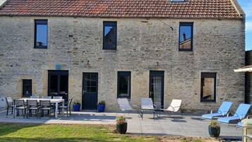 Ein Steinhaus mit Ziegeldach, einer Terrasse mit Sitzgelegenheiten und einem kleinen Garten.