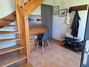 A wooden staircase leading to a loft bedroom with a desk and chair, a coat rack, and a radiator. - Holiday Home 'Longues Amarres' with Terrace, Garden and Wi-Fi (Longues-sur-Mer)