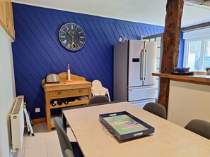 Een kleine keuken met een blauwe wand, een klok, een koelkast en een eettafel met een dienblad.