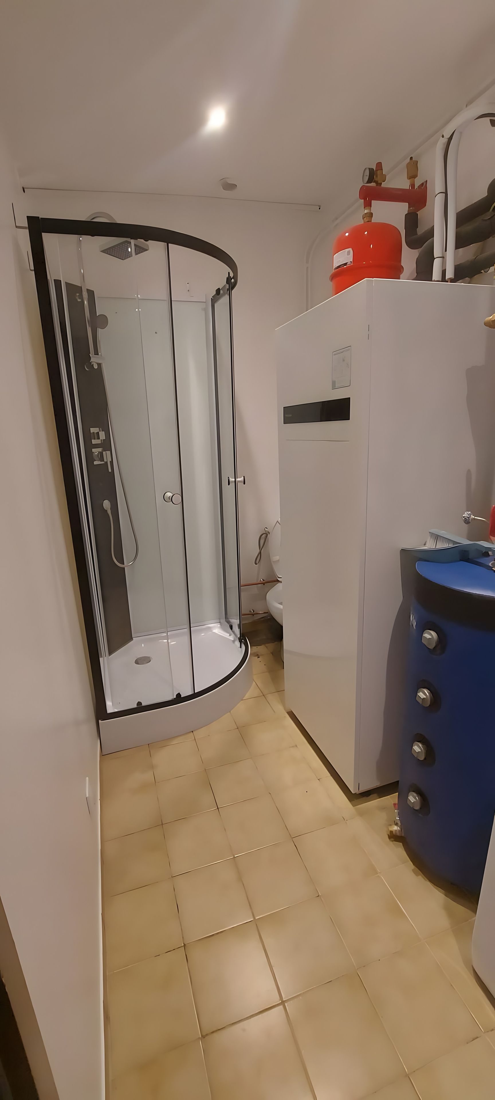 A bathroom with a glass shower enclosure, a white toilet, and a blue cabinet with knobs.