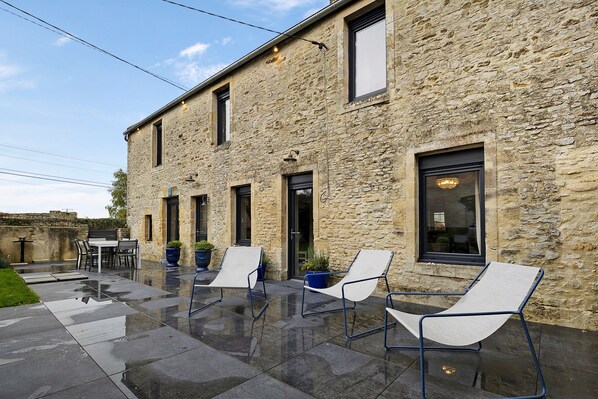 A stone building with a patio area featuring two lounge chairs and a table.