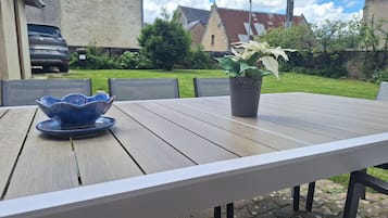 Une terrasse extérieure avec une table en bois, des chaises, une plante en pot et un bol bleu.