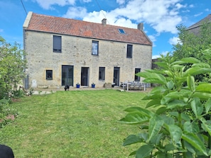 A stone building with a tiled roof, a grassy yard, and a table with chairs. - Holiday Home 'Longues Amarres' with Terrace, Garden and Wi-Fi (Longues-sur-Mer)