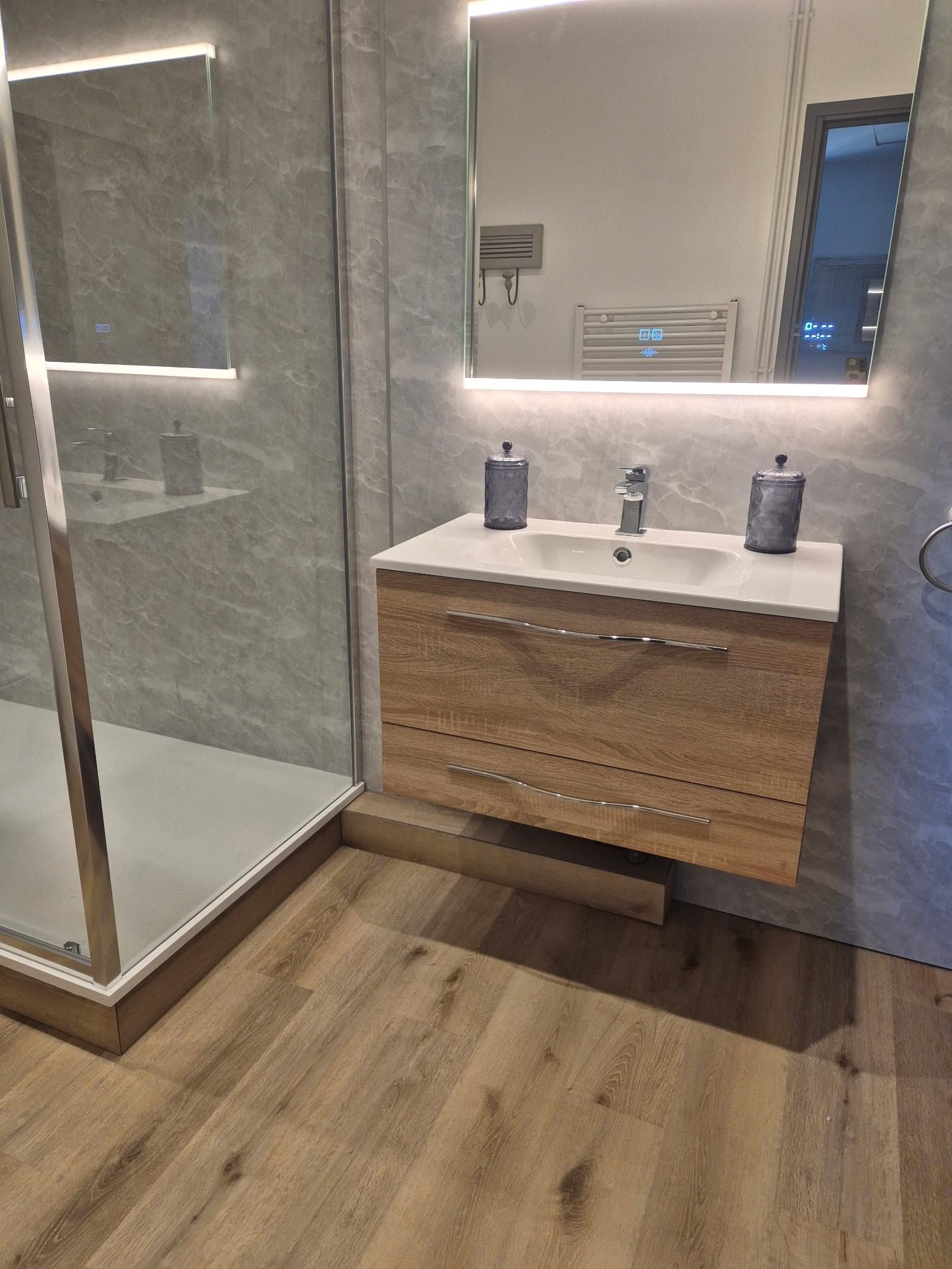 Un bagno moderno con box doccia in vetro, mobile bagno in legno con lavandino e specchio.