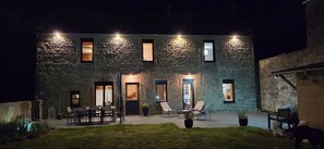 A stone building with multiple windows and doors, outdoor seating area with chairs and tables, and potted plants. - Holiday Home 'Longues Amarres' with Terrace, Garden and Wi-Fi (Longues-sur-Mer)