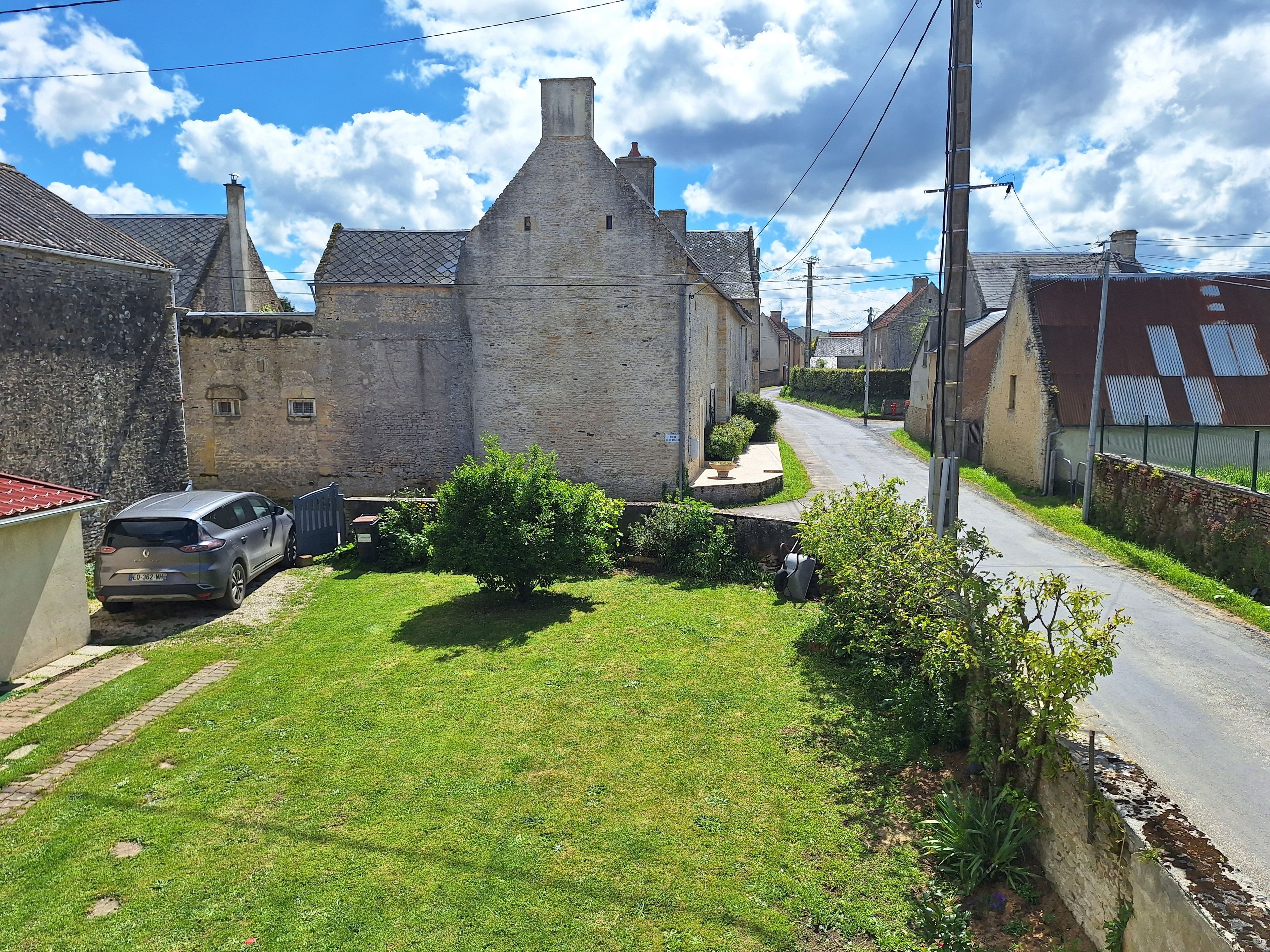 A residential street with stone buildings, a parked car, and a grassy area.