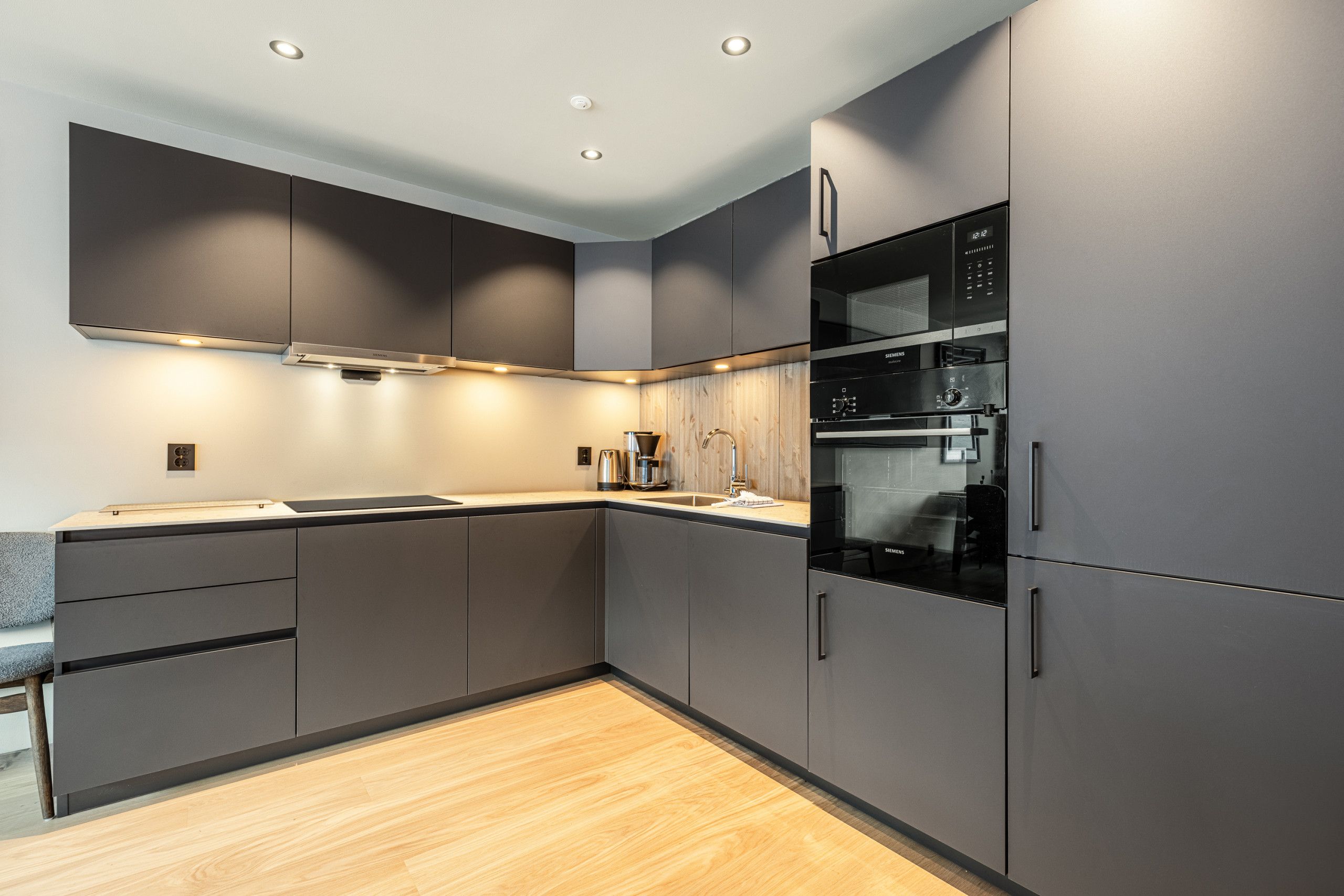 A modern kitchen with built-in appliances, grey cabinetry, and a wooden floor.