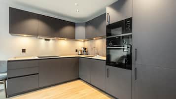 A modern kitchen with built-in appliances, grey cabinetry, and a wooden floor.
