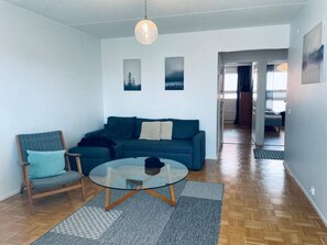 A living room with a sofa, a chair, a glass coffee table, and a hanging light fixture.