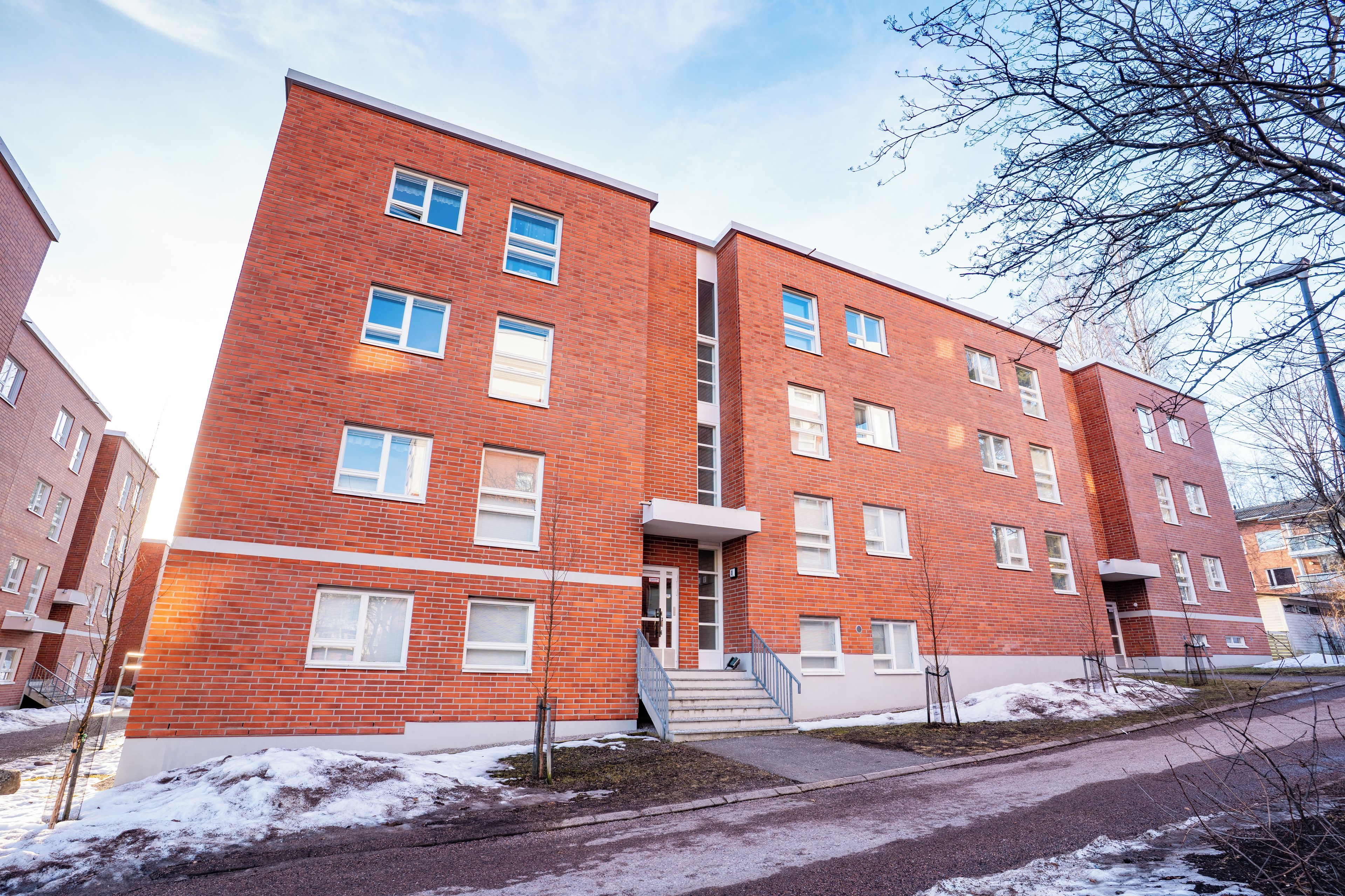 En byggnad i flera våningar, byggd av tegel, med en central trappa, fönster och en liten trädgårdsyta.