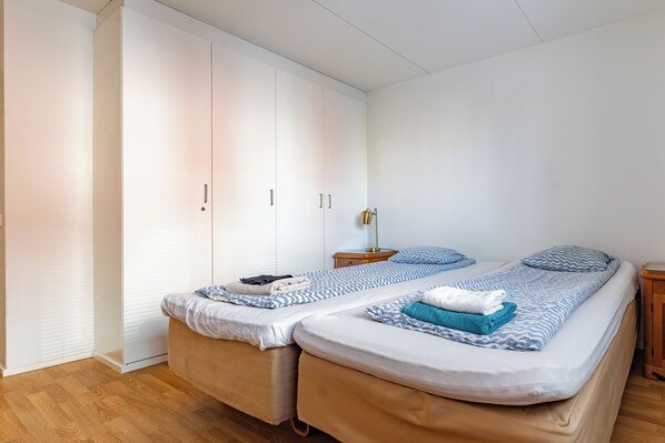 A bedroom with two beds, a wardrobe, a bedside table, and a lamp.