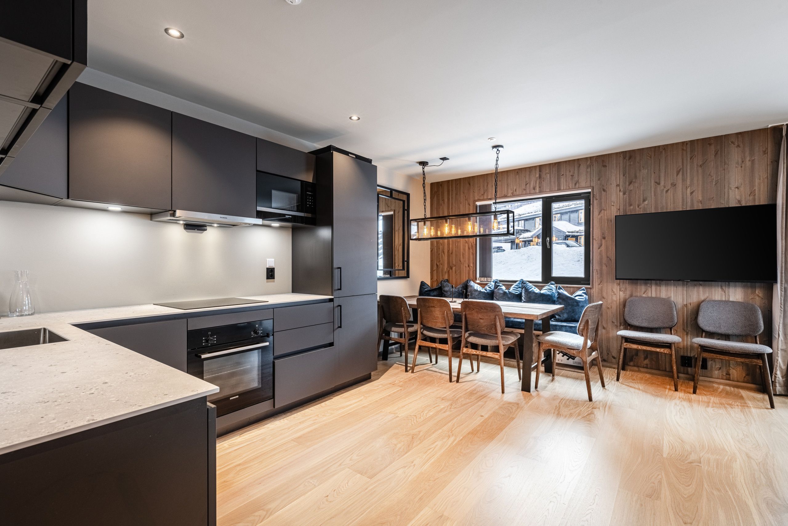 Une cuisine moderne avec un coin repas, un plancher en bois et une grande fenêtre.