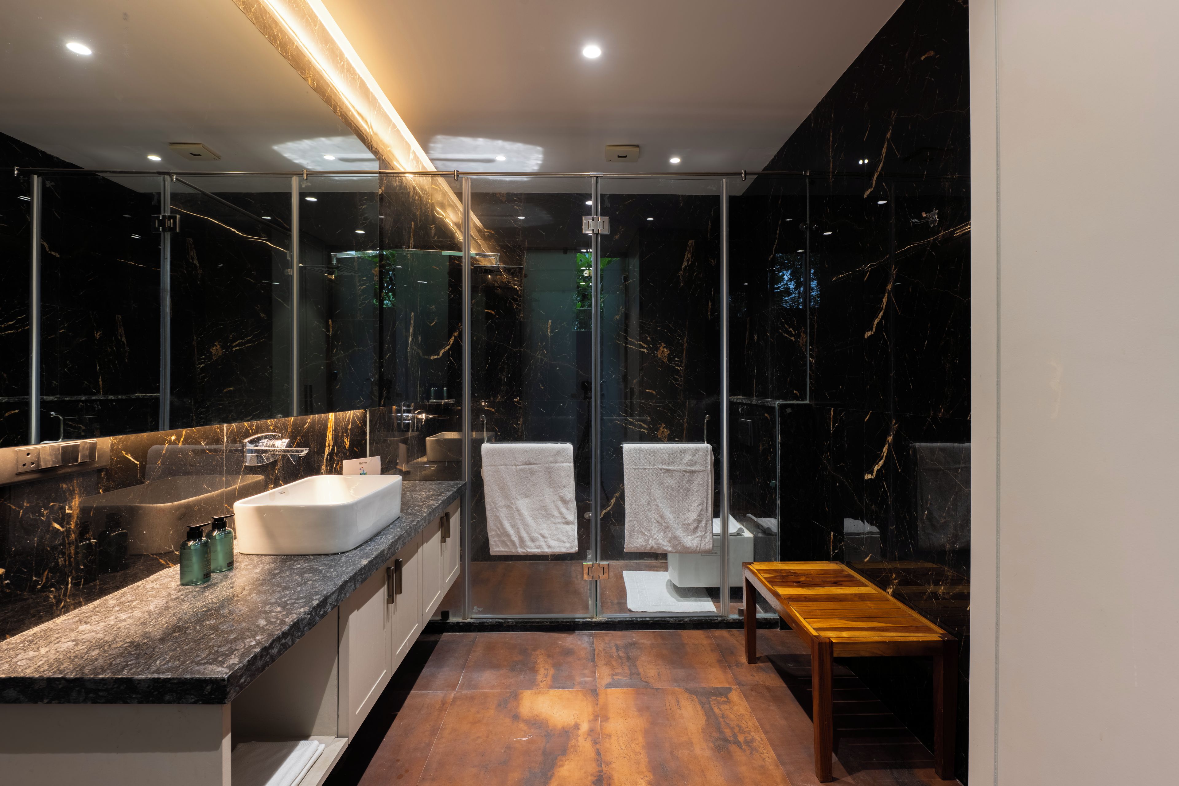 A modern bathroom with a marble vanity, a glass shower enclosure, and a wooden bench.