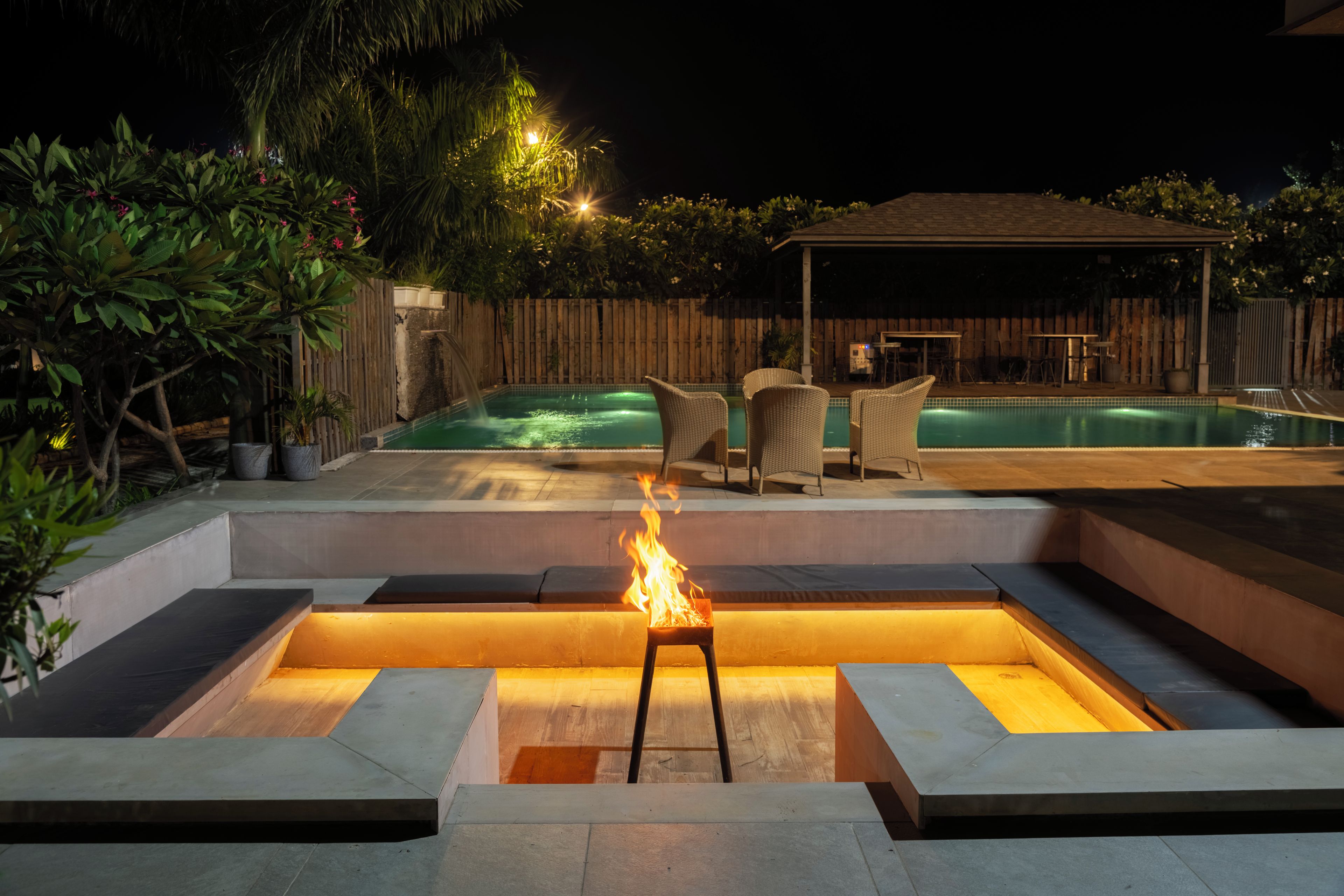 A backyard with a swimming pool, outdoor seating, and a fire feature.
