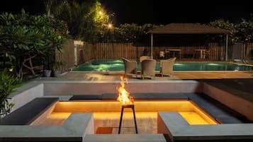 A backyard with a swimming pool, outdoor seating, and a fire feature.