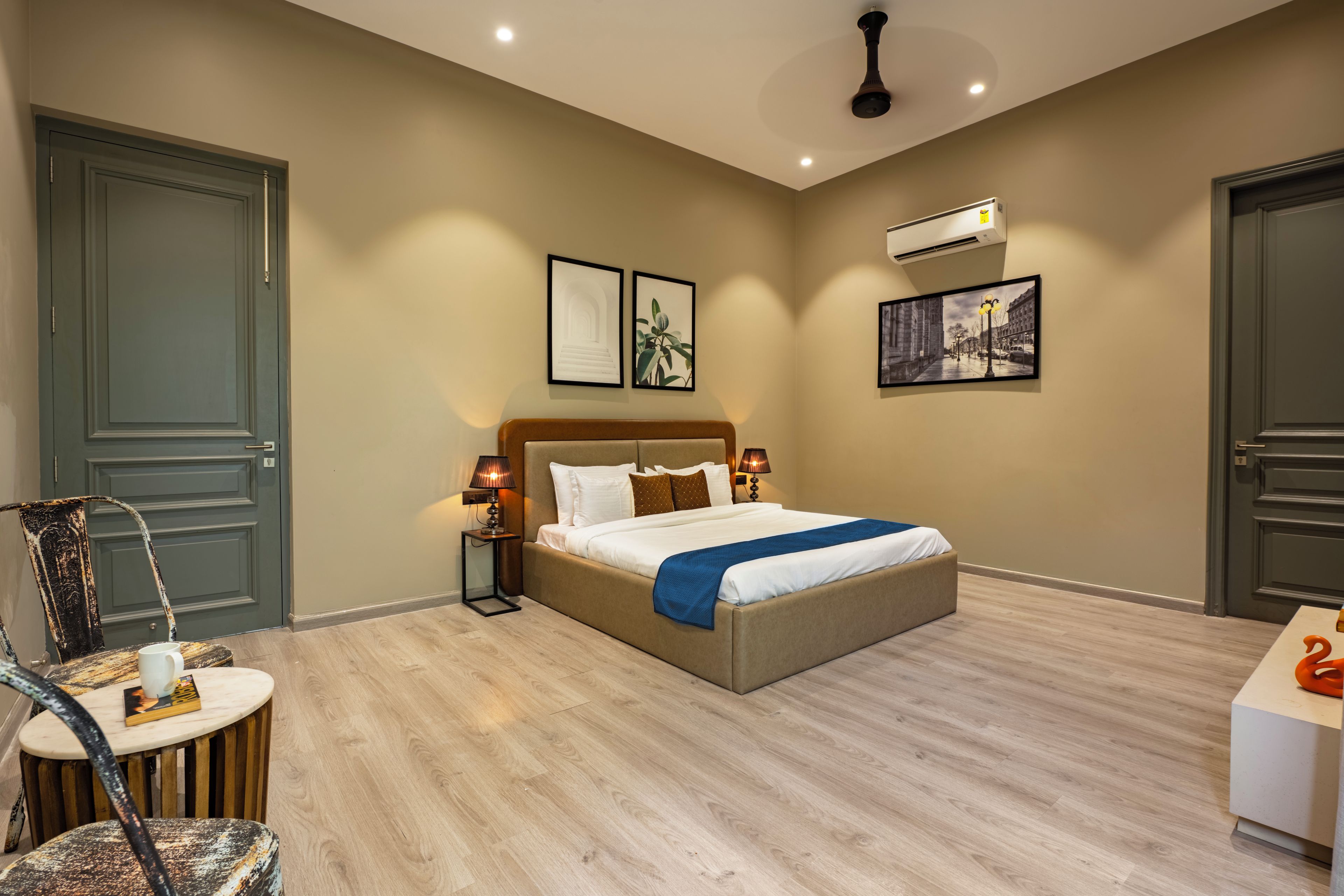 A hotel room with a bed, two bedside lamps, a wall-mounted air conditioner, and two framed pictures.