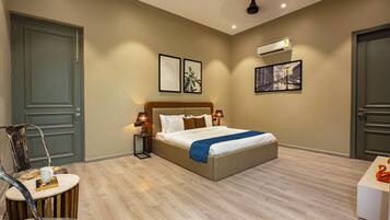 A hotel room with a bed, two bedside lamps, a wall-mounted air conditioner, and two framed pictures.