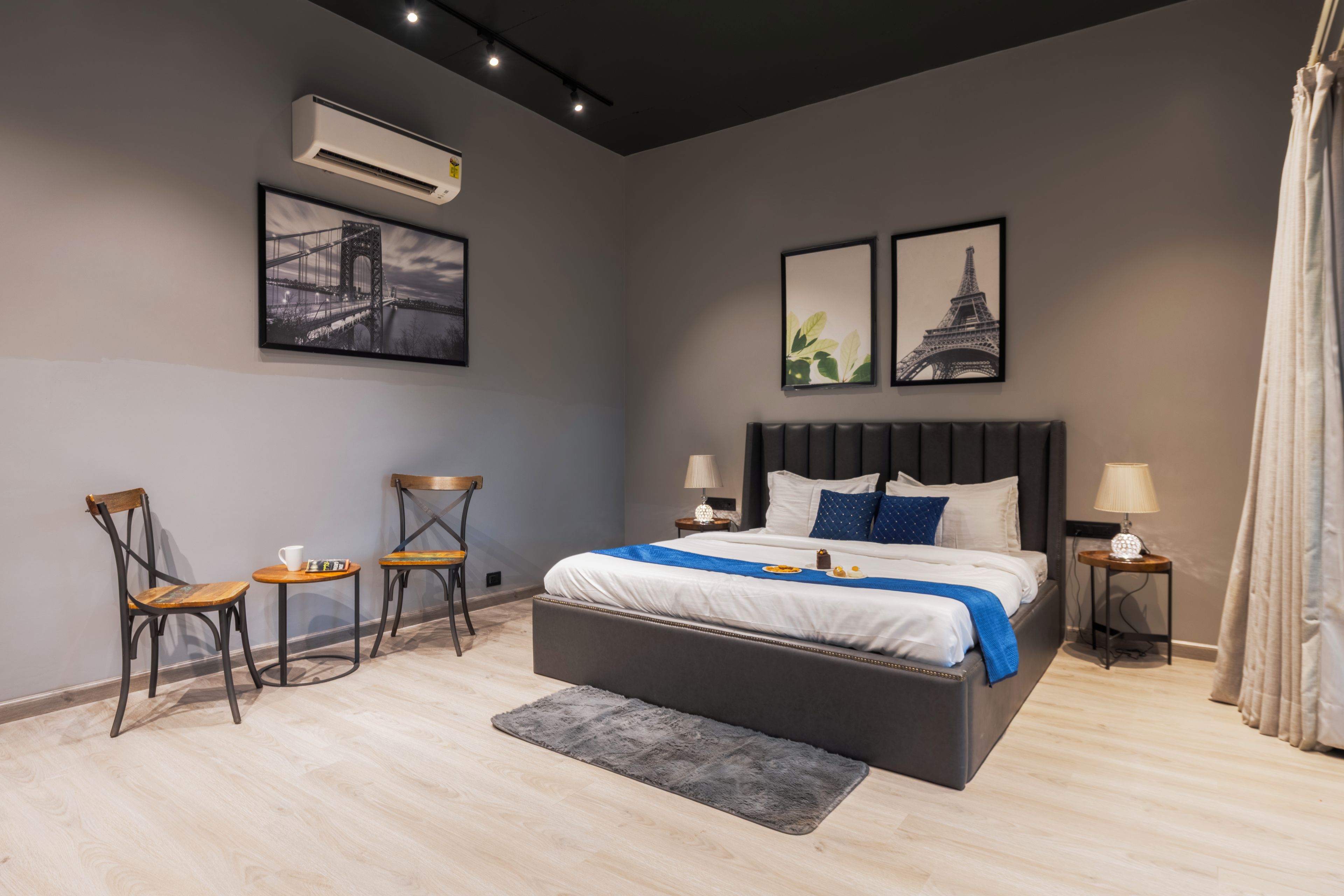 Ein modernes Schlafzimmer mit einem großen Bett, zwei Stühlen, einem kleinen Tisch und Kunstwerken an den Wänden.