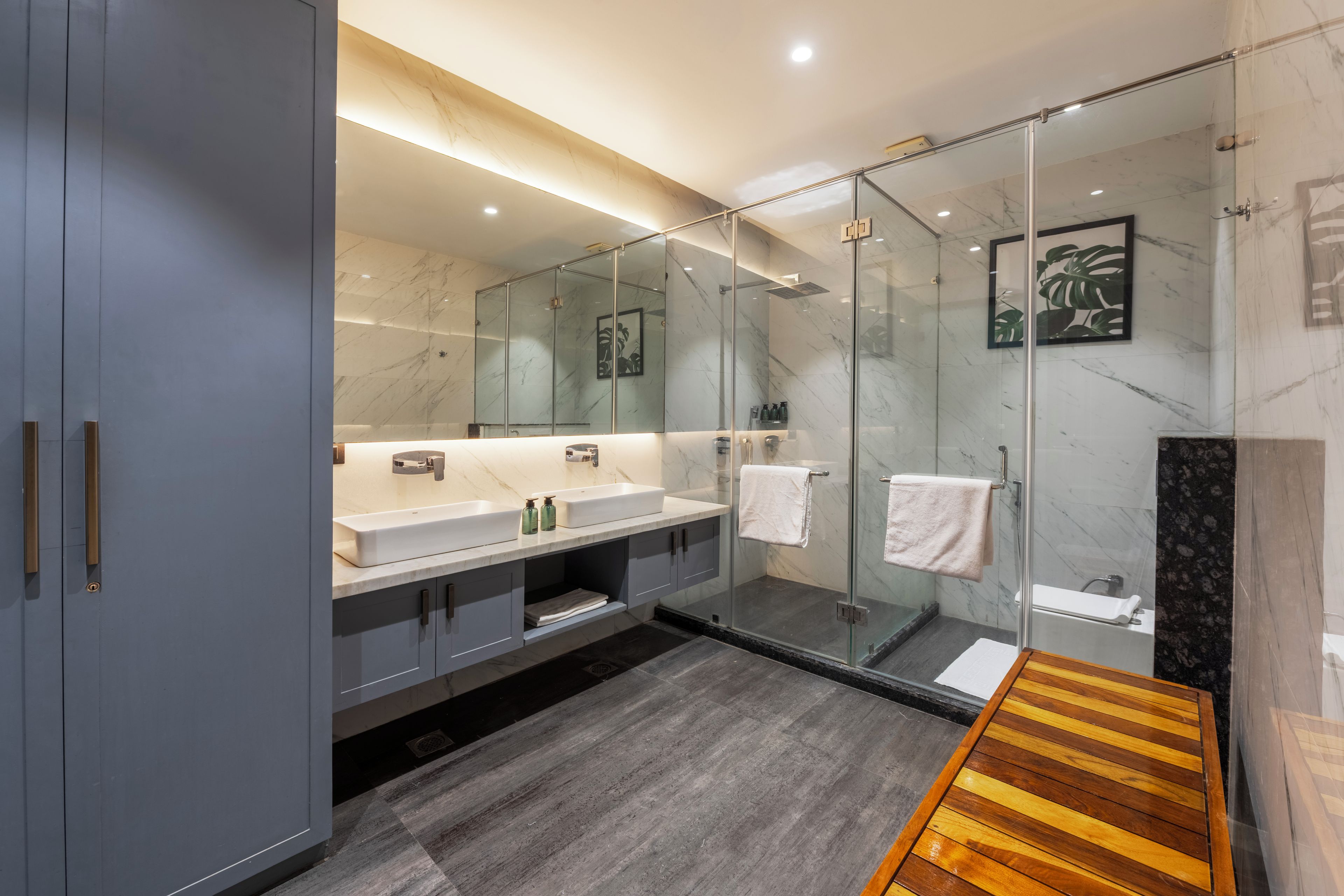 A modern bathroom with a glass-enclosed shower, dual sinks, and a wooden bench.