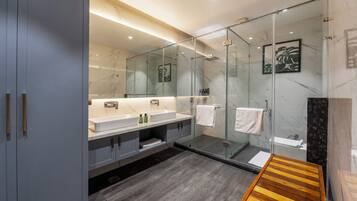 A modern bathroom with a glass-enclosed shower, dual sinks, and a wooden bench.