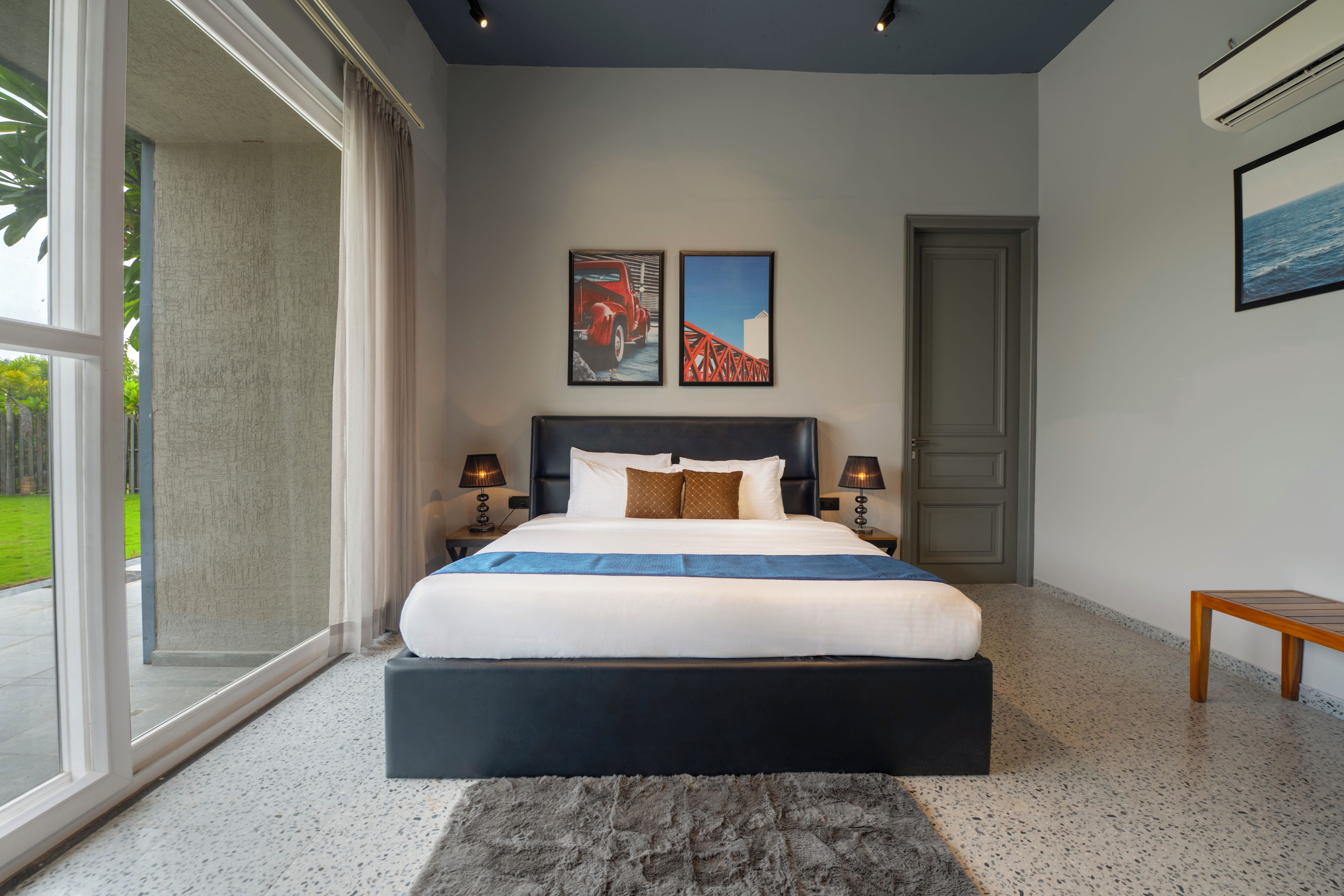 Une chambre moderne avec un grand lit, deux tables de chevet avec des lampes, une porte et deux tableaux encadrés accrochés au mur.