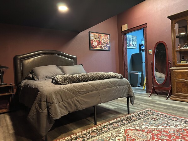 A bedroom with a bed, a wooden dresser, a mirror, and a rug.