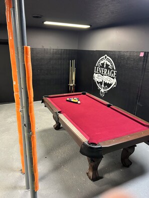 A pool table with balls, a cue stick, and a wall with a logo.