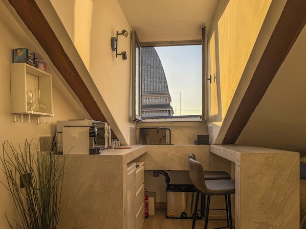 A compact kitchen with a window view, a coffee machine, and a bar stool. - Mole House (Torino)